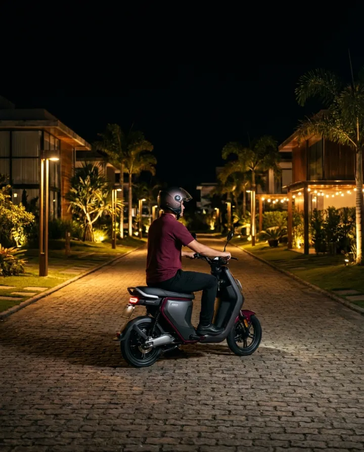 Colaborador de polo bordô em uma moto elétrica percorrendo a rua interna iluminada de um condomínio à noite